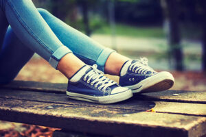 Young woman in jeans and blue sneakers on a bench in the park