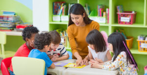 Asian female teacher teaching mixed race kids reading book in classroom,Kindergarten pre school concept.