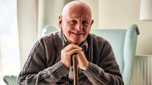 Portrait of happy senior man sitting at home with walking stock and smiling