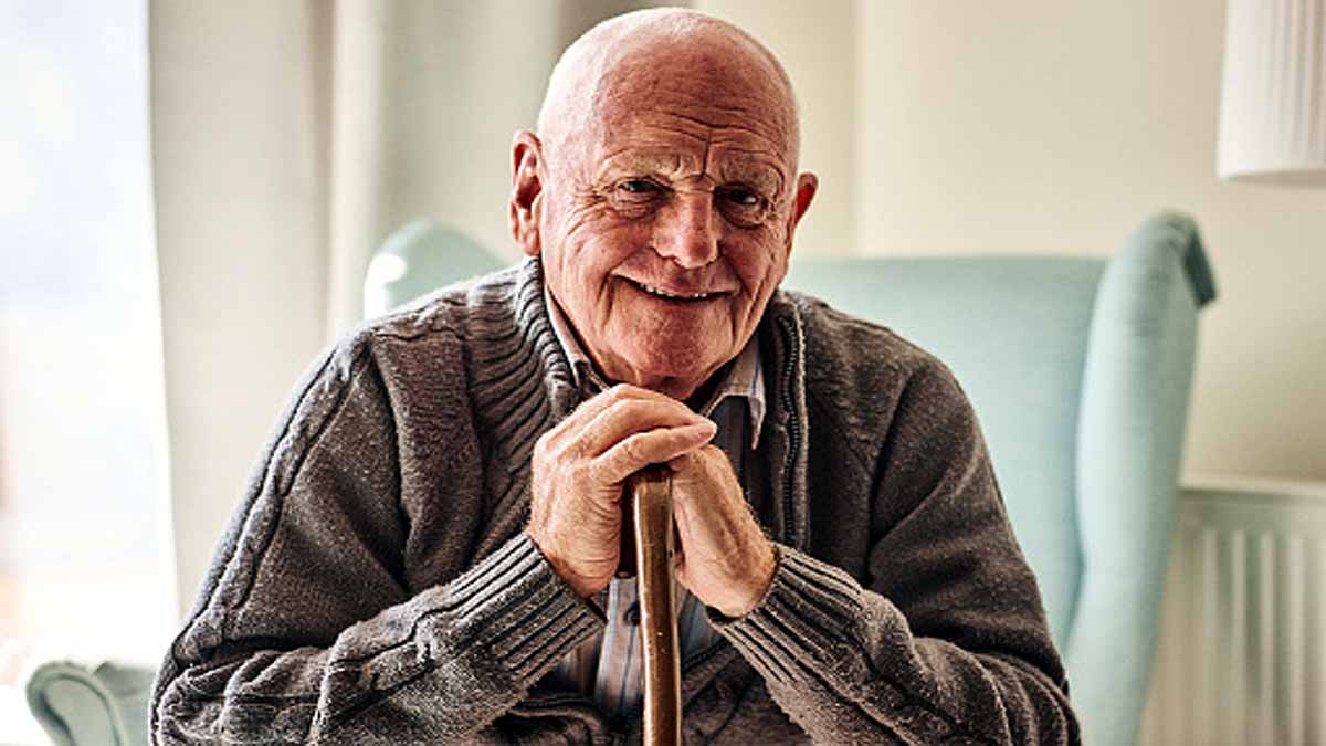 Portrait of happy senior man sitting at home with walking stock and smiling